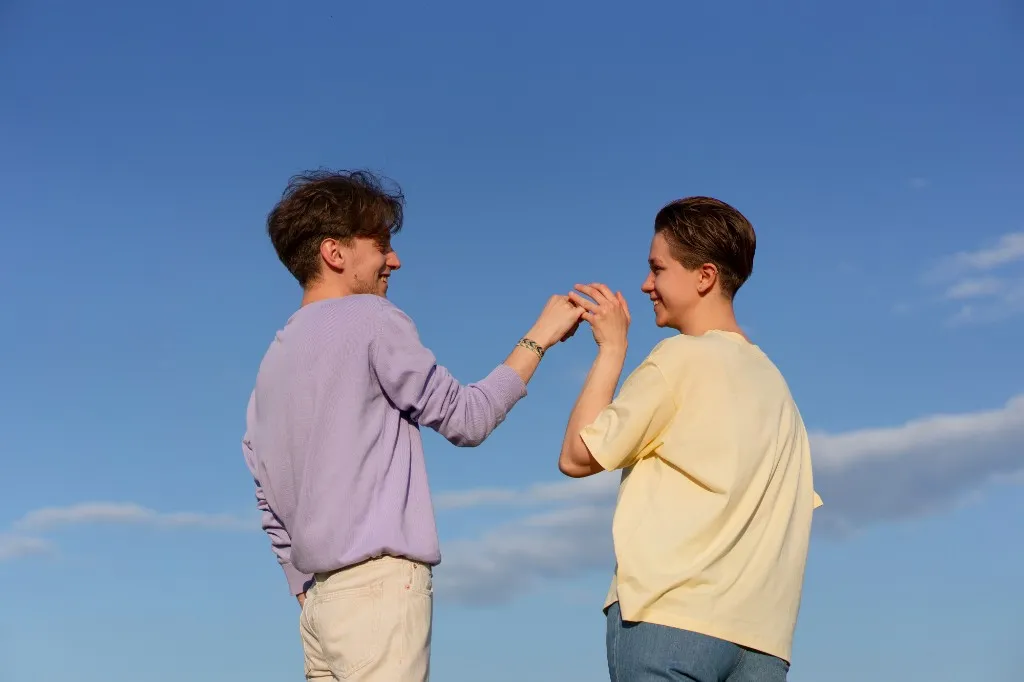 Two young people outdoors, pinky swear, smiling against a blue sky